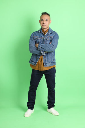 The 40s adult Asian man with jean shirt standing on the green background.の写真素材