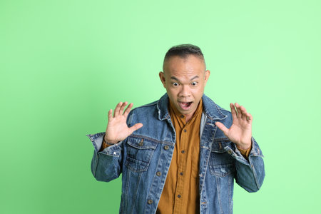 The 40s adult Asian man with jean shirt standing on the green background.