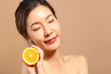 The beautiful  Asian woman showing skin with brown background holding fruit.の写真素材