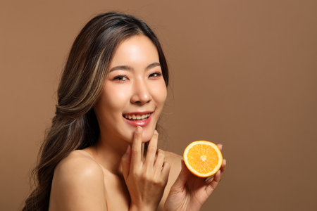 The beautiful  Asian woman showing skin with brown background holding lemon.の写真素材