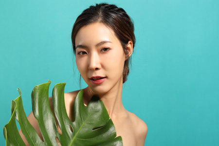 The beautiful  Asian woman showing skin with green background holding monsteras leaf.の写真素材