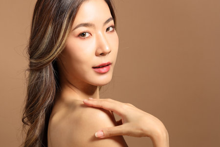 The beautiful  Asian woman showing skin with brown background holding monstera leaf.の写真素材