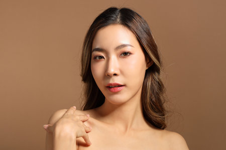 The beautiful  Asian woman showing skin with brown background holding monstera leaf.の写真素材