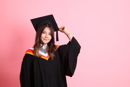 The Asian woman in graduation gown standing on the pink background.の写真素材