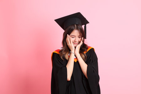 The Asian woman in graduation gown standing on the pink background.の写真素材