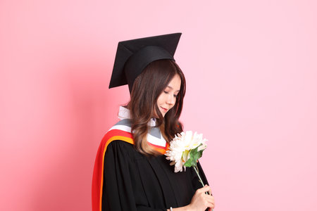 The Asian woman in graduation gown standing on the pink background.の写真素材