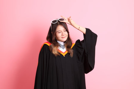 The Asian woman in graduation gown standing on the pink background.の写真素材