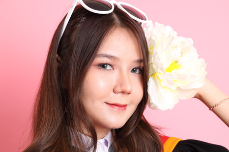 The Asian woman in graduation gown standing on the pink background.の写真素材
