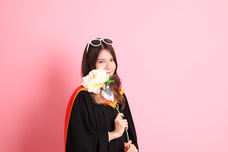 The Asian woman in graduation gown standing on the pink background.の写真素材