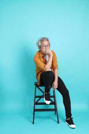 The attractive senior Asian man with yellow shirt sitting on the green background.