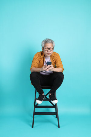 The attractive senior Asian man with yellow shirt standing on the green background.
