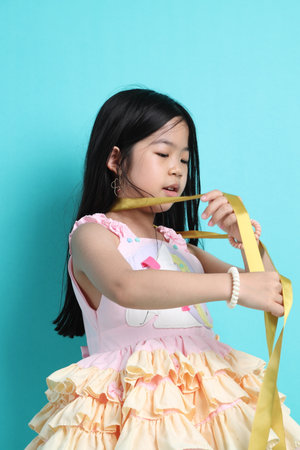 The little Asian girl playing with ribbon on the green background.