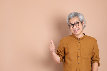 The 40s adult Asian man with yellow shirt standing on the brown background.の写真素材