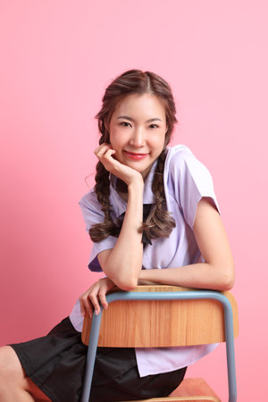 The Asian girl in Thai student uniform sitting on the chair in the pink background.の写真素材