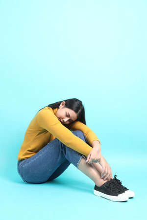 The Asian woman in casual clothes sitting on the green background.