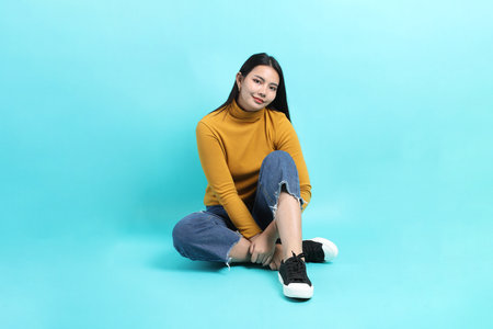 The Asian woman in casual clothes sitting on the green background.