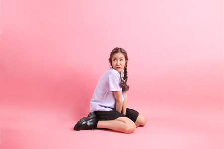 The Asian girl in Thai student uniform sitting on the pink background.の写真素材