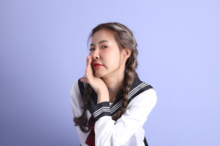 The Asian girl in Japanese student uniform standing on the purple background.の写真素材