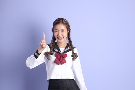 The Asian girl in Japanese student uniform standing on the purple background.の写真素材