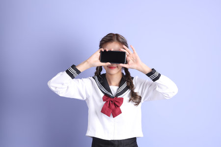 The Asian girl in Japanese student uniform standing on the purple background.の写真素材