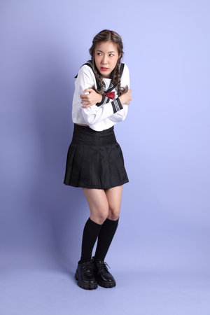 The Asian girl in Japanese student uniform standing on the purple background.の写真素材