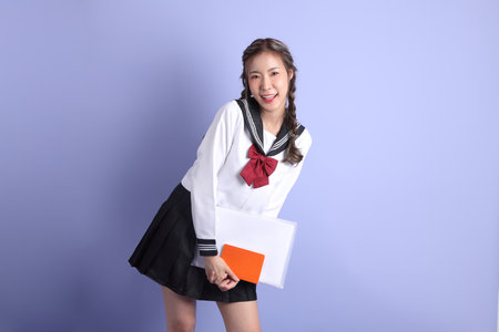 The Asian girl in Japanese student uniform standing on the purple background.の写真素材