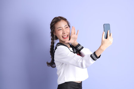 The Asian girl in Japanese student uniform standing on the purple background.の写真素材
