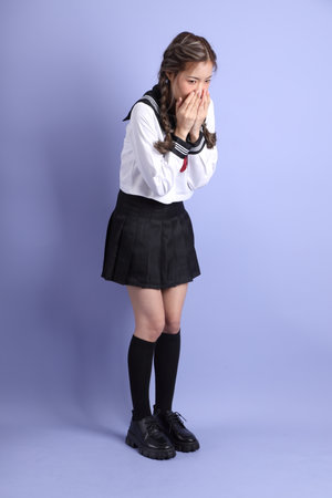The Asian girl in Japanese student uniform standing on the purple background.の写真素材