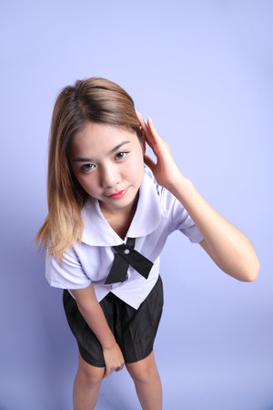 The Asian girl in Thai student uniform standing on the purple background.の写真素材