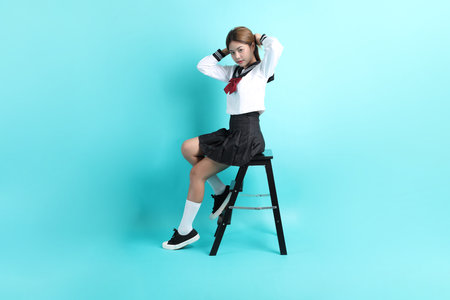 The Asian girl in Japanese student uniform sitting on the chair on the green background.の写真素材