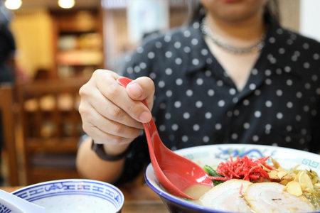 The Asian woman eating ramen in the restaurant.