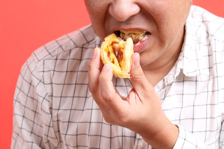 The Asian man eating egg tart on the orange background.の写真素材
