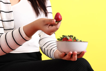 The Asian woman holding strawberry in the hand on the yellow background.の写真素材
