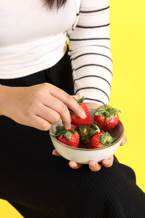 The Asian woman holding strawberry in the hand on the yellow background.の写真素材