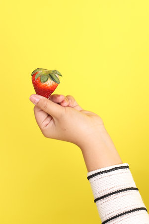 The Asian woman holding strawberry in the hand on the yellow background.の写真素材
