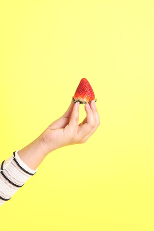The Asian woman holding strawberry in the hand on the yellow background.の写真素材