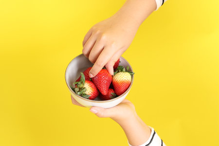 The Asian woman holding strawberry in the hand on the yellow background.の写真素材