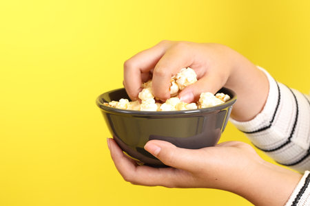 The Asian woman holding popcorn in the hand on the yellow background.の写真素材