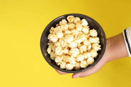 The Asian woman holding popcorn in the hand on the yellow background.の写真素材