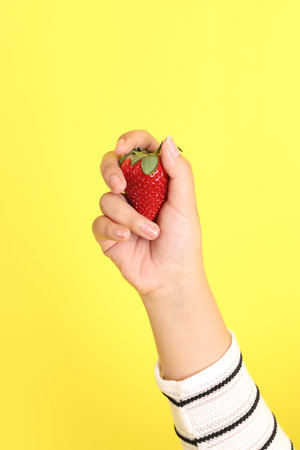 The Asian woman holding strawberry in the hand on the yellow background.の写真素材