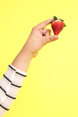 The Asian woman holding strawberry in the hand on the yellow background.の写真素材