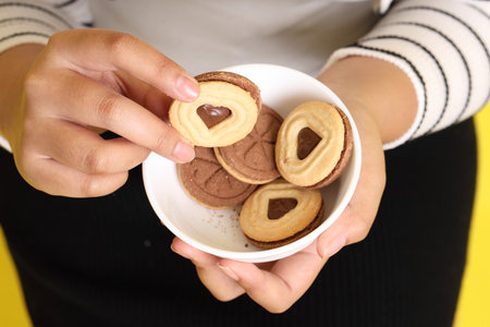 The Asian woman holding cookies in the hand on the yellow background.