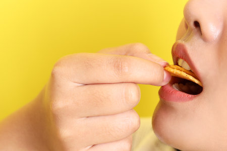 The Asian woman eating potato chips from the hand on the yellow background.