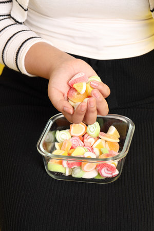 The Asian woman holding jelly in the hand on the yellow background.