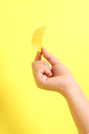 The Asian woman holding potato chips in the hand on the yellow background.の写真素材