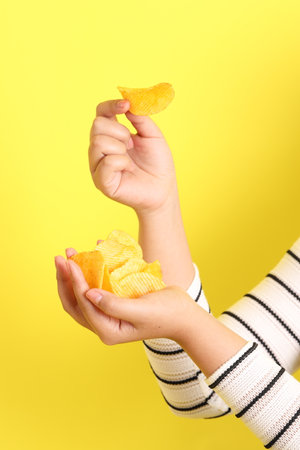 The Asian woman holding potato chips in the hand on the yellow background.の写真素材