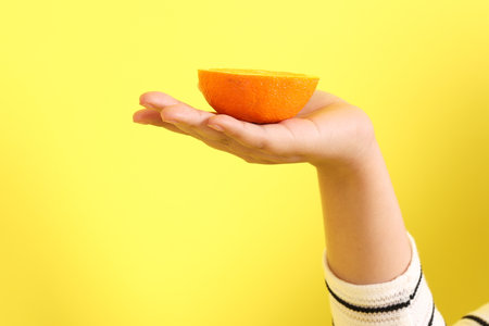 The Asian woman holding orange in the hand on the yellow background.の写真素材