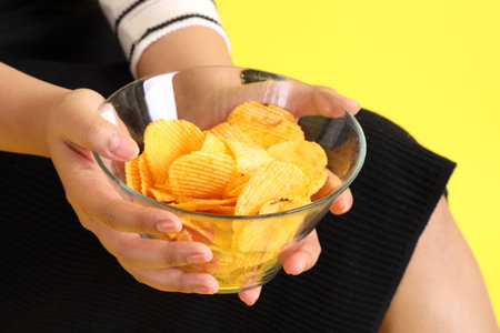 The Asian woman holding potato chips in the hand on the yellow background.の写真素材