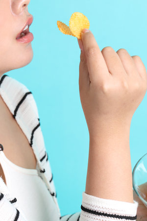 The Asian woman eating potato chips from the hand on the yellow background.の写真素材