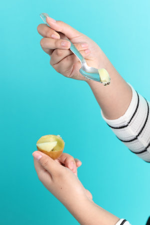 The Asian woman holding kiwi fruit in the hand on the grenn background.